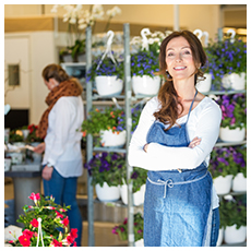 Portrait of smiling mid adult female owner with customers in background at flower shop