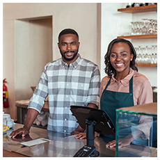 Portrait of two young African entrepreneurs smiling and standing welcomingly together behind the counter of their trendy cafe
